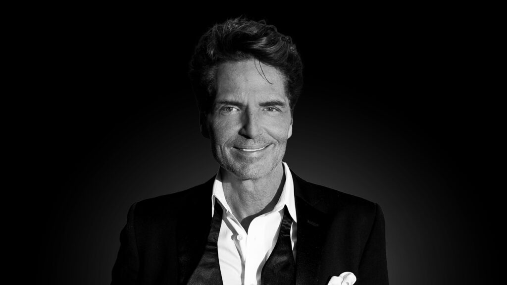 Singer Richard Marx in a suit, posing against a dark backdrop.