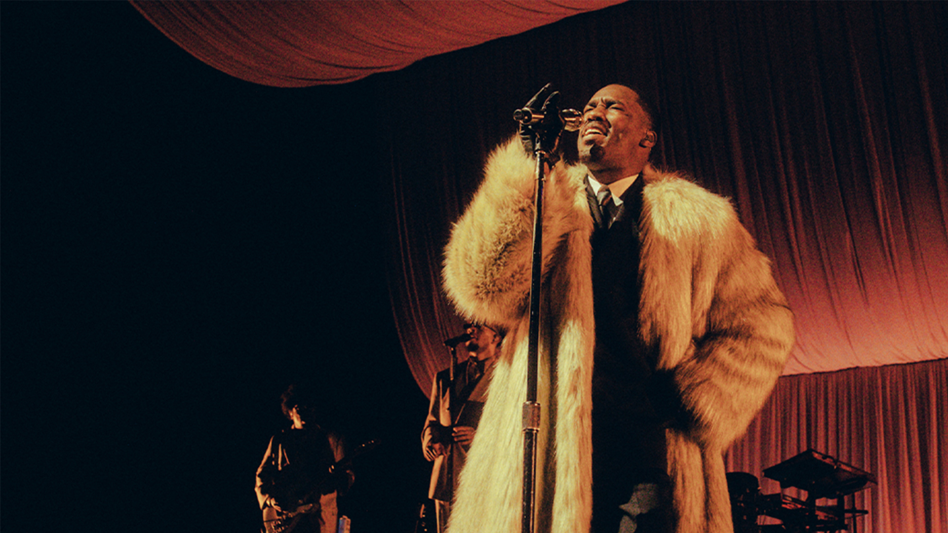 Singer GIVĒON dressed in a suit and fur coat, singing on stage.
