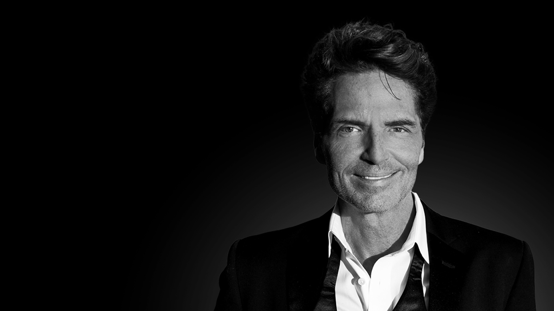 Singer Richard Marx in a suit, posing against a dark backdrop.