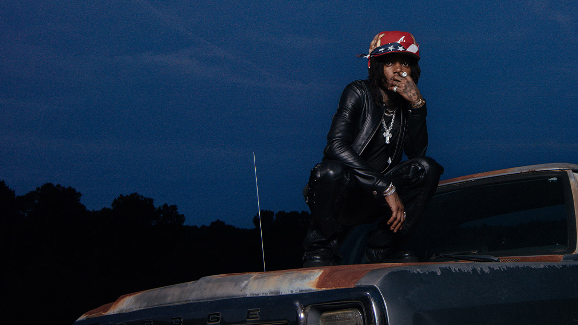 J.I.D posing, seated on the top of a car.