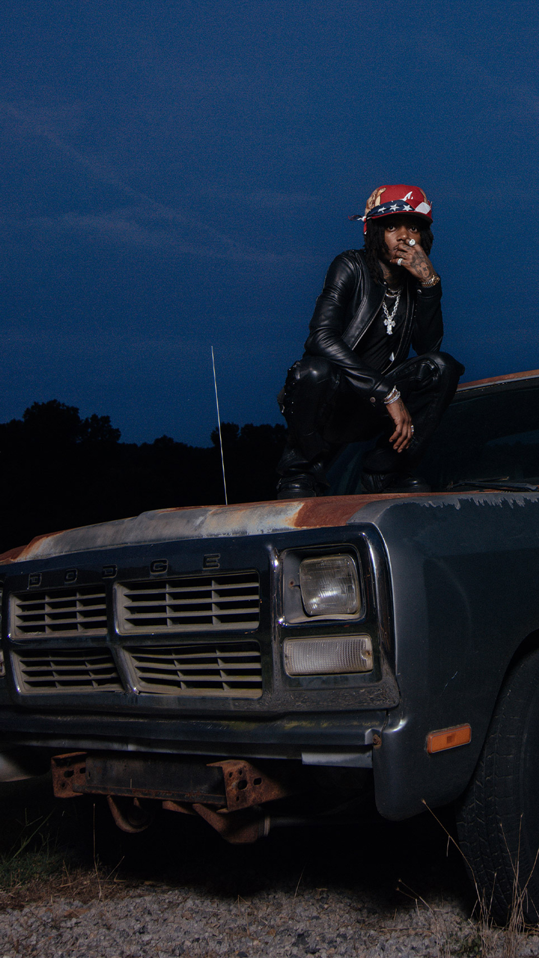J.I.D posing, seated on the top of a car.