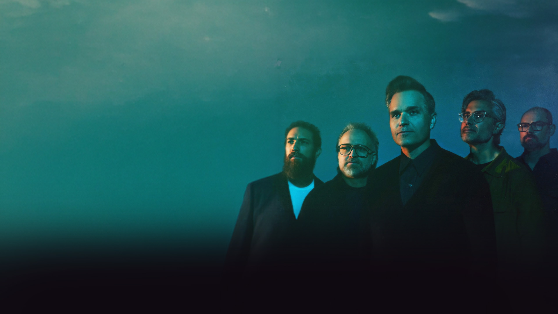 Death Cab For Cutie band members dressed in black and posing against a blue background.