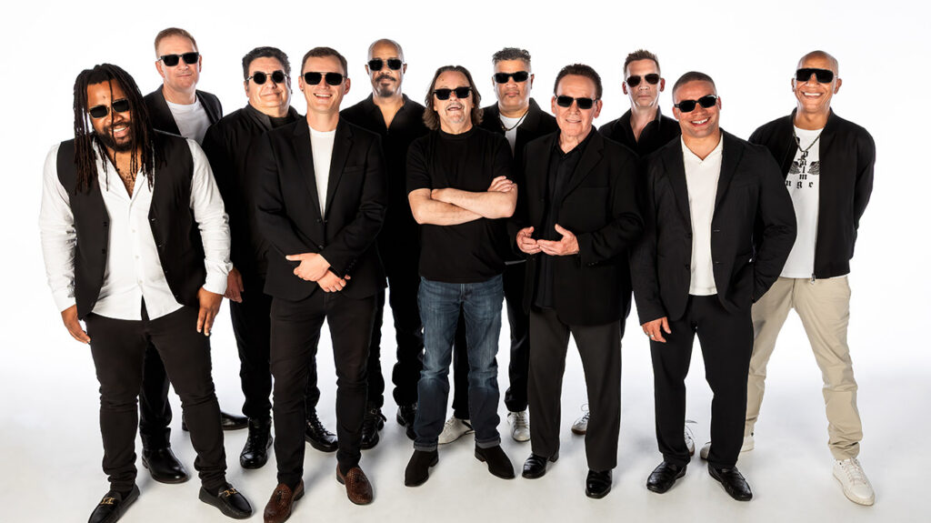 UB40 band members pose together in casual clothing and black sunglasses.