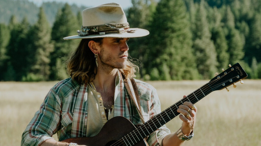 The lead singer of KALEO, a man in a cowboy hat, performs while playing an acoustic guitar.