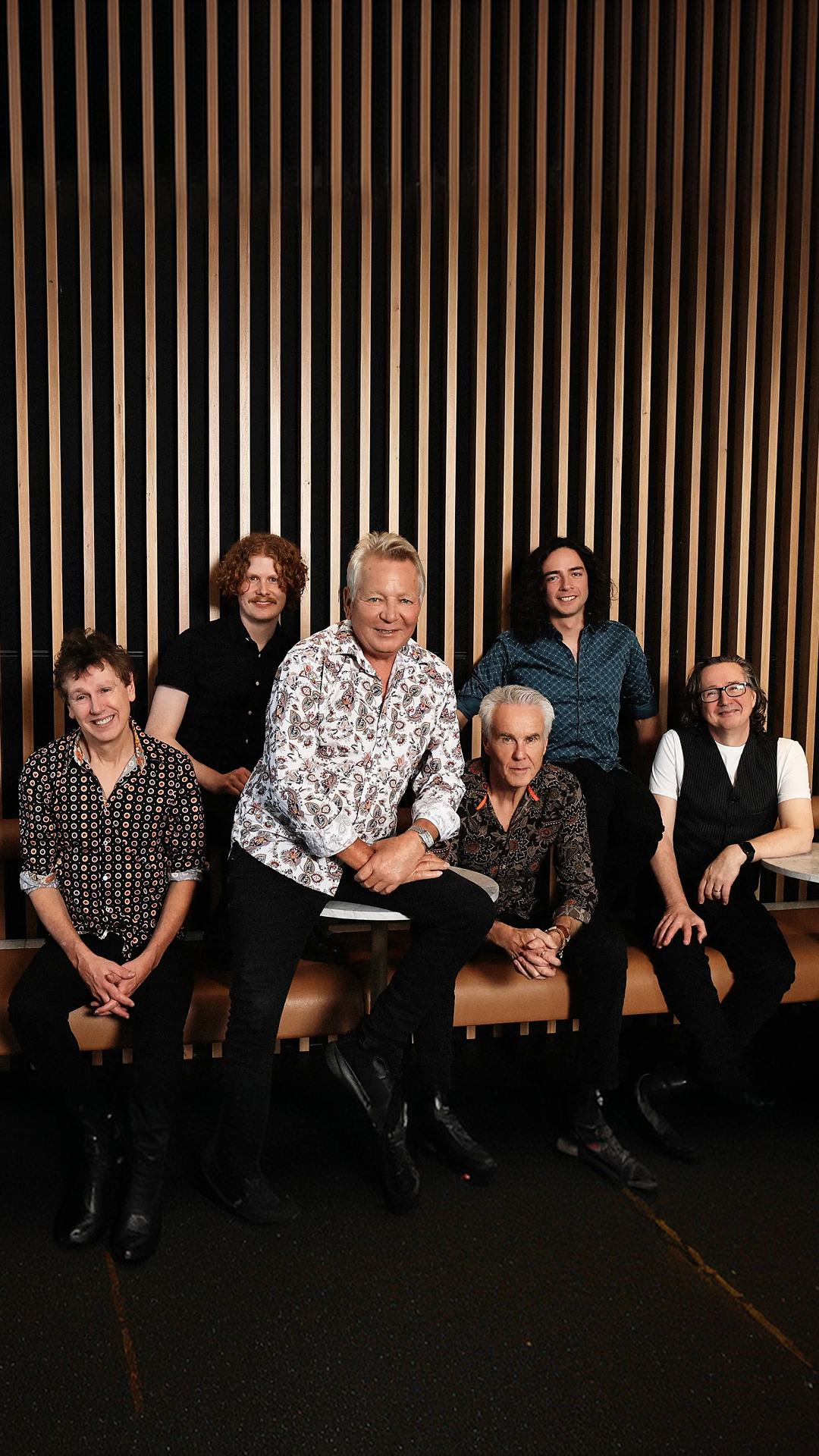 Icehouse band members posing in a room with a wooden wall backdrop.